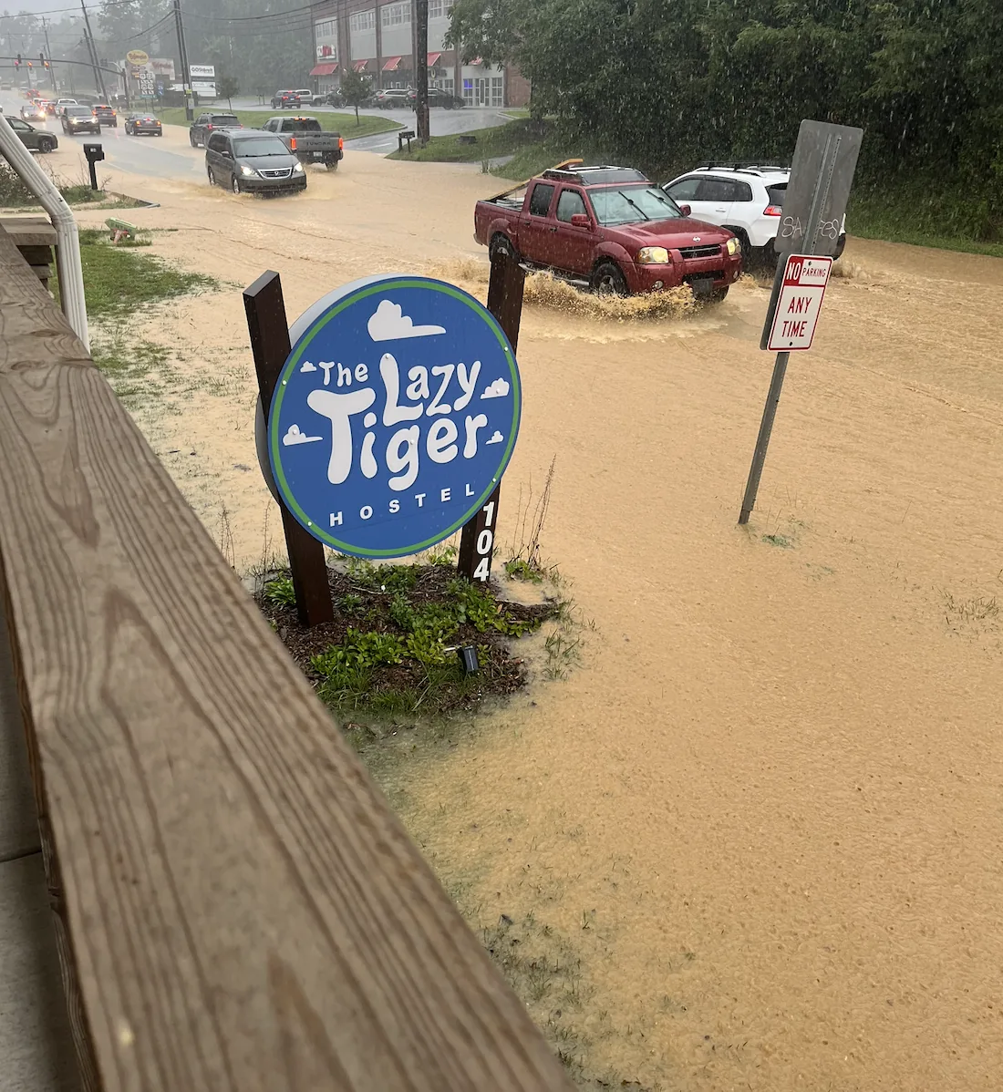 Floodwater covering the street and entrance beside the Lazy Tiger Hostel sign during a July storm
